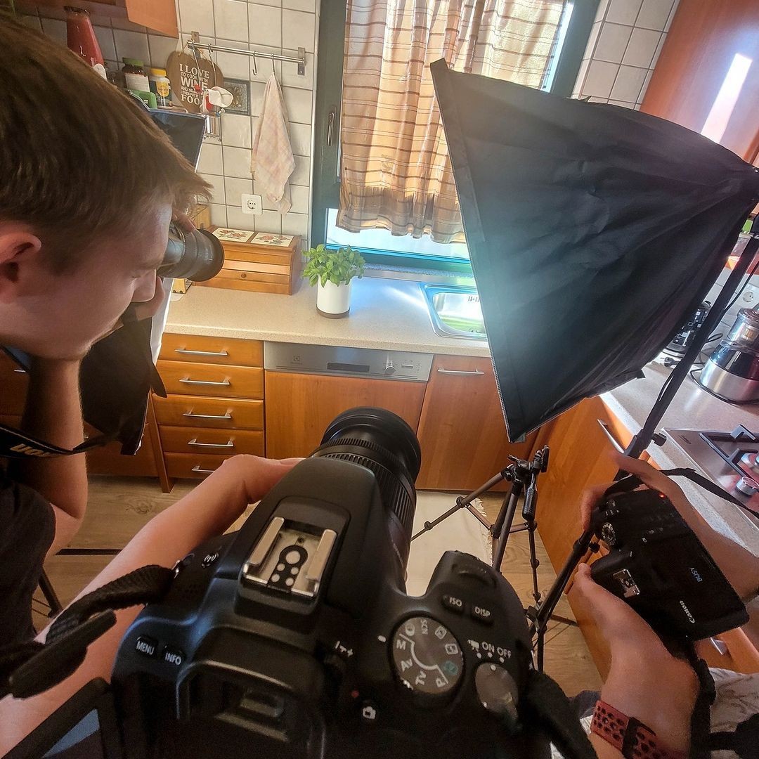 Photographers setting up cameras and lighting equipment to photograph a potted plant in a kitchen.